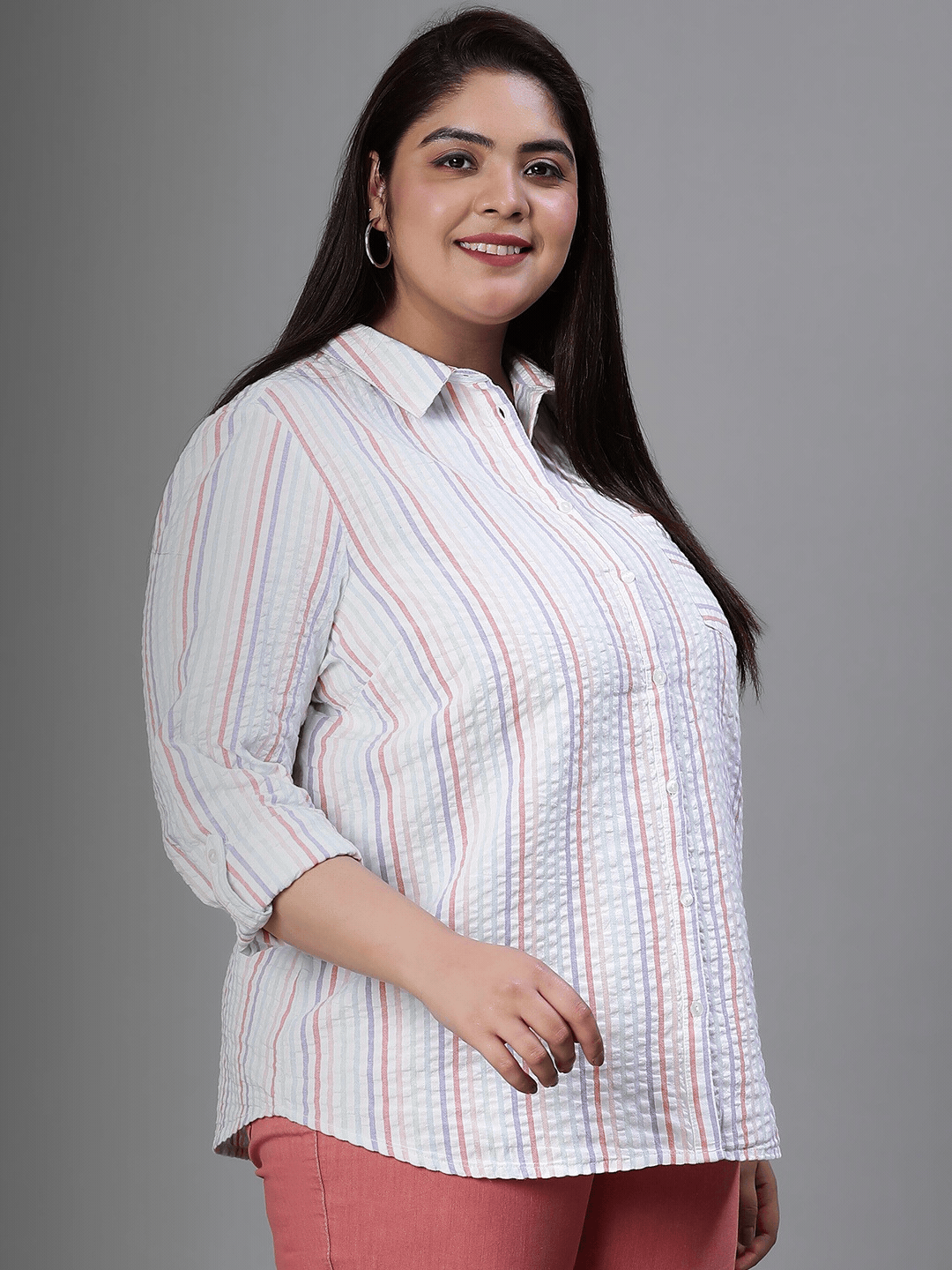 A woman wearing a striped shirt and pink pants is standing next to a white stool.