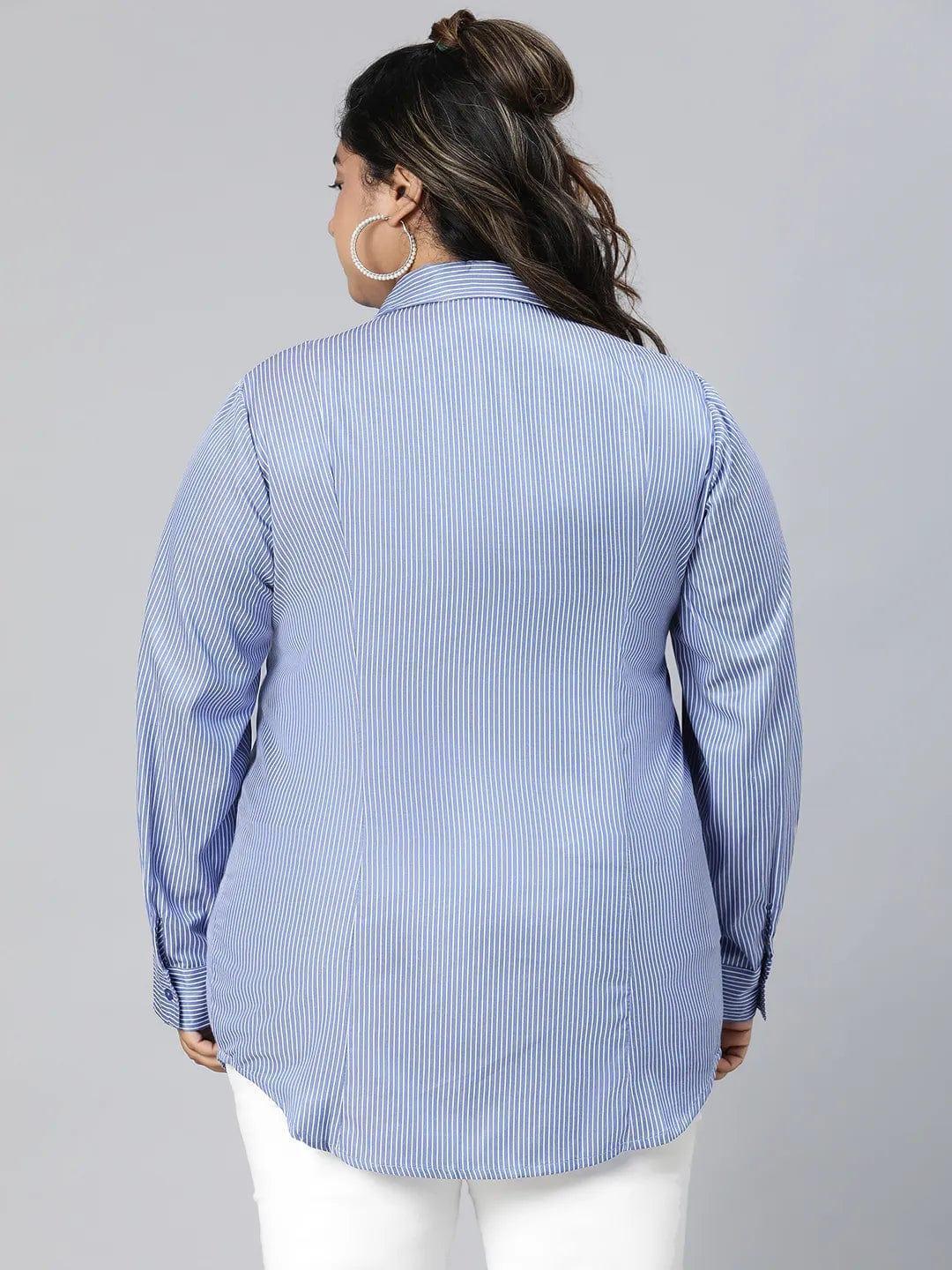 A woman with long brown hair wearing a blue striped button-up shirt and white pants, smiling at the camera.
