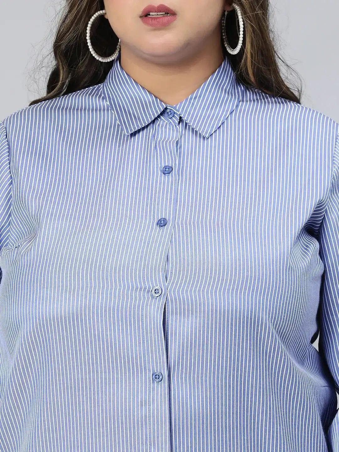 A woman with long brown hair wearing a blue striped button-up shirt and white pants, smiling at the camera.