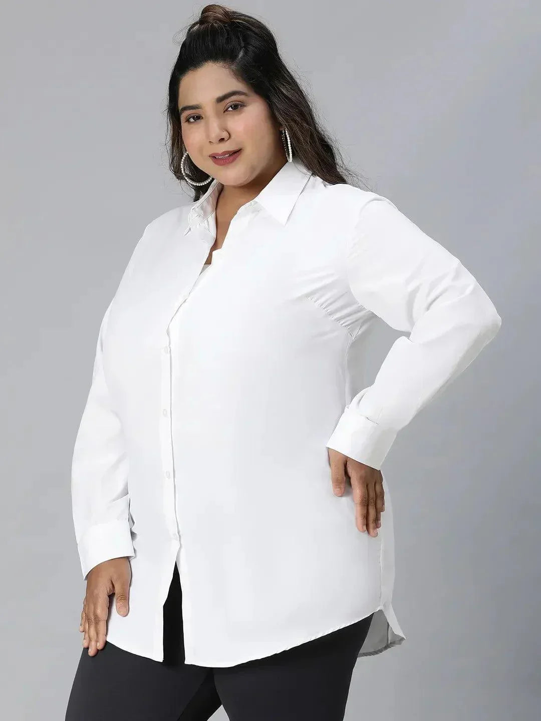 A woman with long dark hair wearing a white button-up shirt and black pants is smiling at the camera.