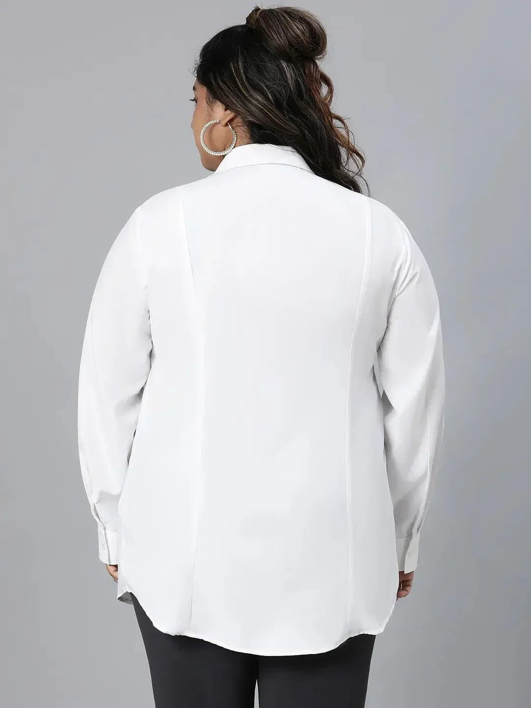A woman with long dark hair wearing a white button-up shirt and black pants is smiling at the camera.