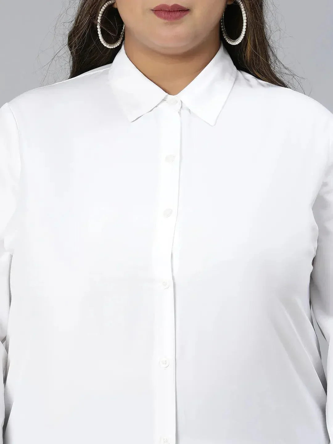 A woman with long dark hair wearing a white button-up shirt and black pants is smiling at the camera.