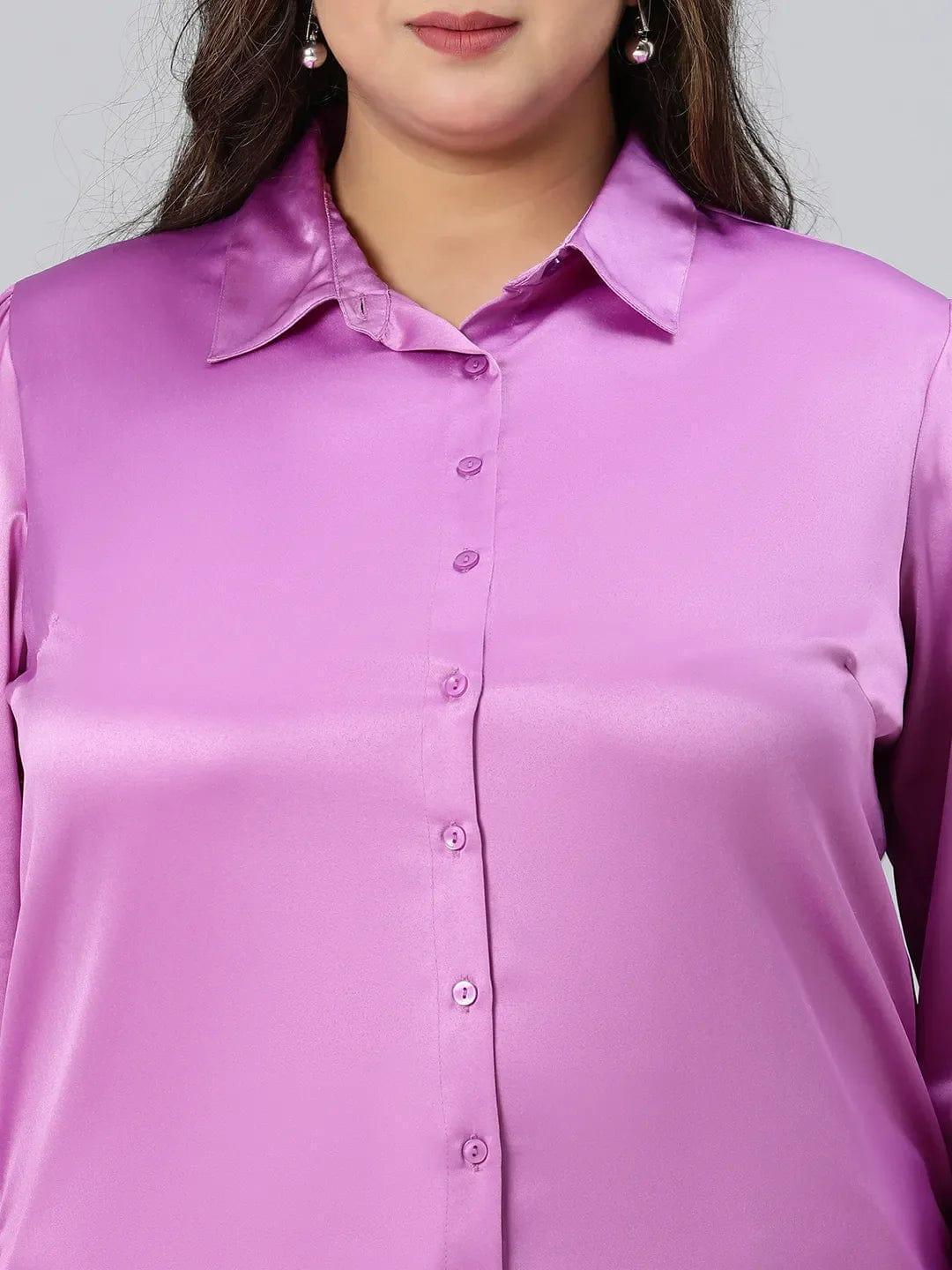 A woman wearing a pink shirt and beige pants is posing with her hand on her head and smiling.