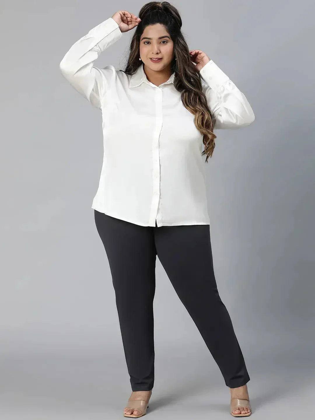 A woman with long brown hair wearing a white blouse and black pants is smiling at the camera.