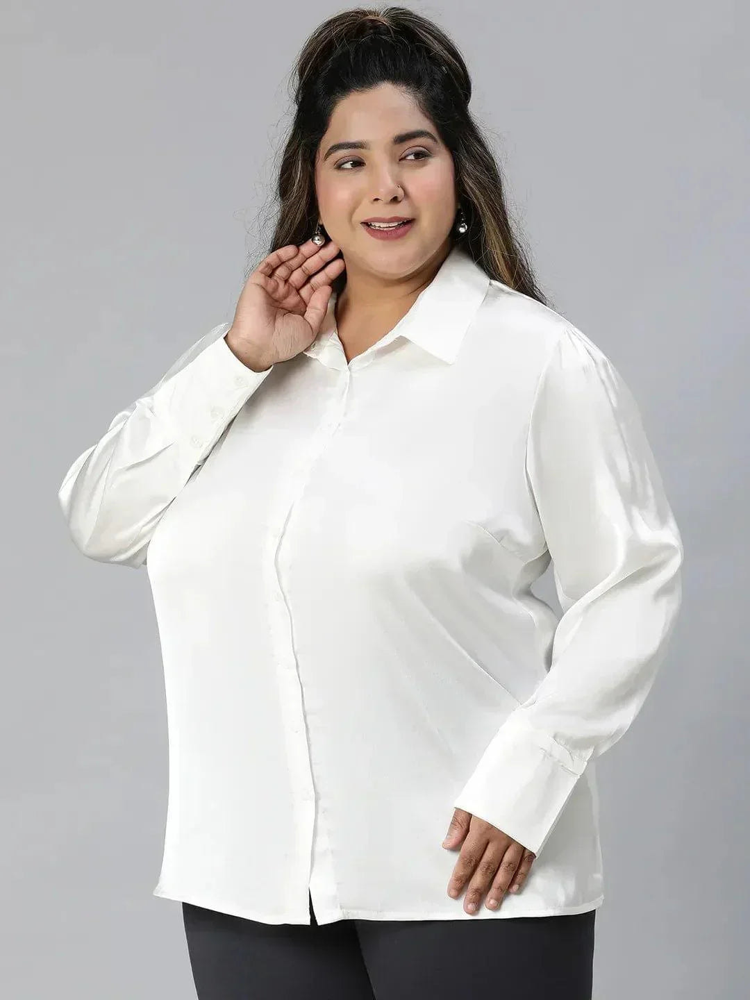 A woman with long brown hair wearing a white blouse and black pants is smiling at the camera.