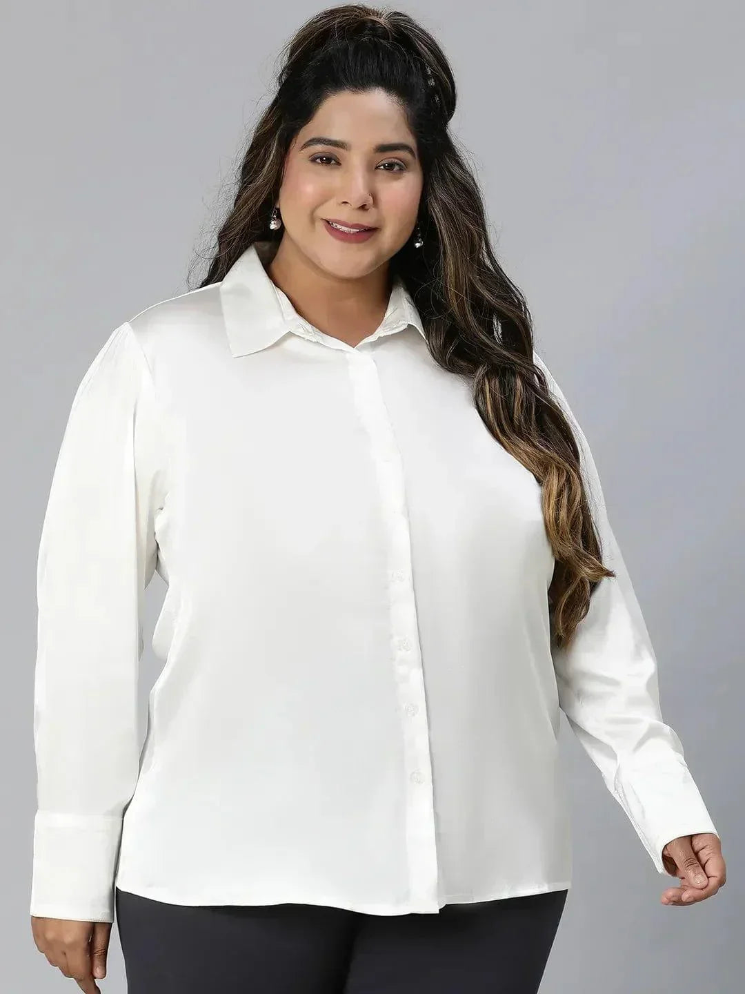 A woman with long brown hair wearing a white blouse and black pants is smiling at the camera.