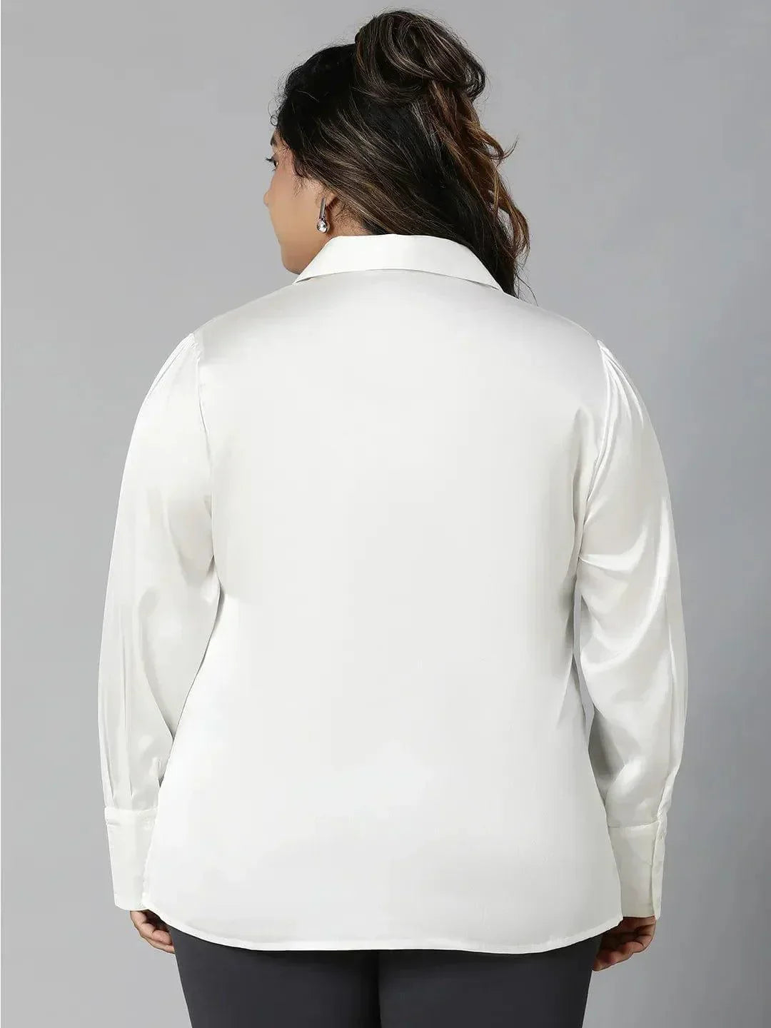 A woman with long brown hair wearing a white blouse and black pants is smiling at the camera.