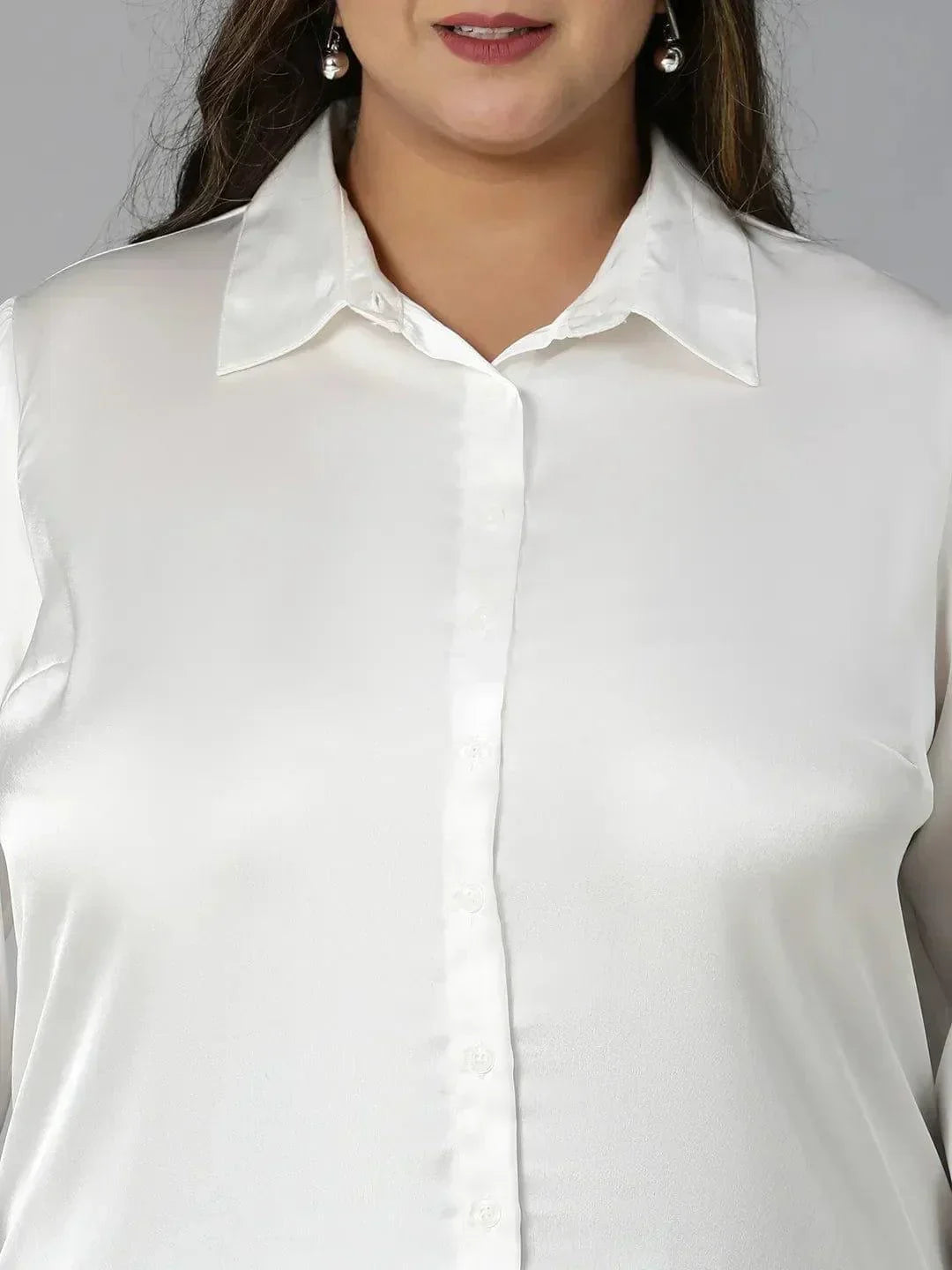 A woman with long brown hair wearing a white blouse and black pants is smiling at the camera.