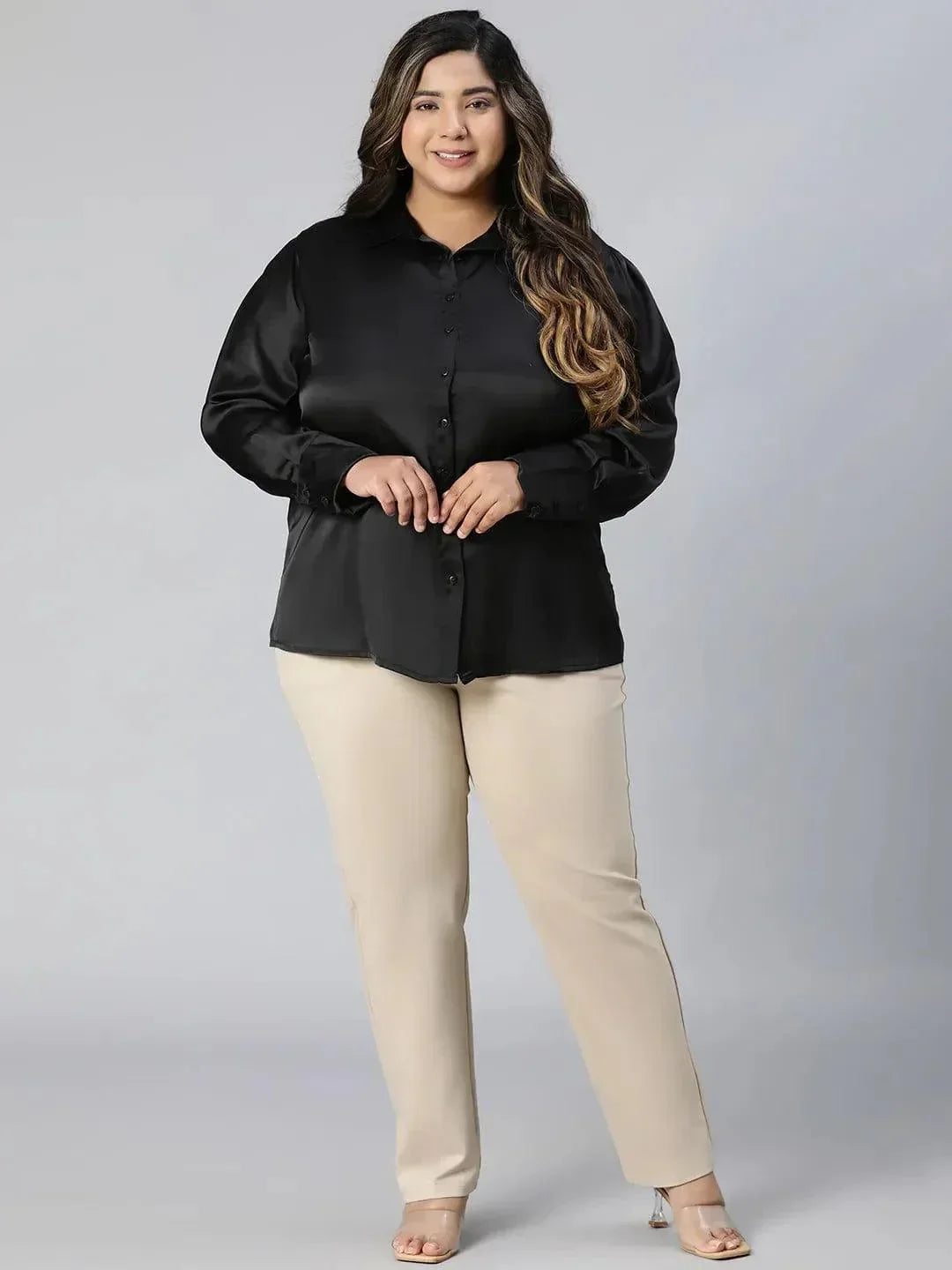 A woman with long, wavy brown hair wearing a black shirt and beige pants, smiling at the camera.