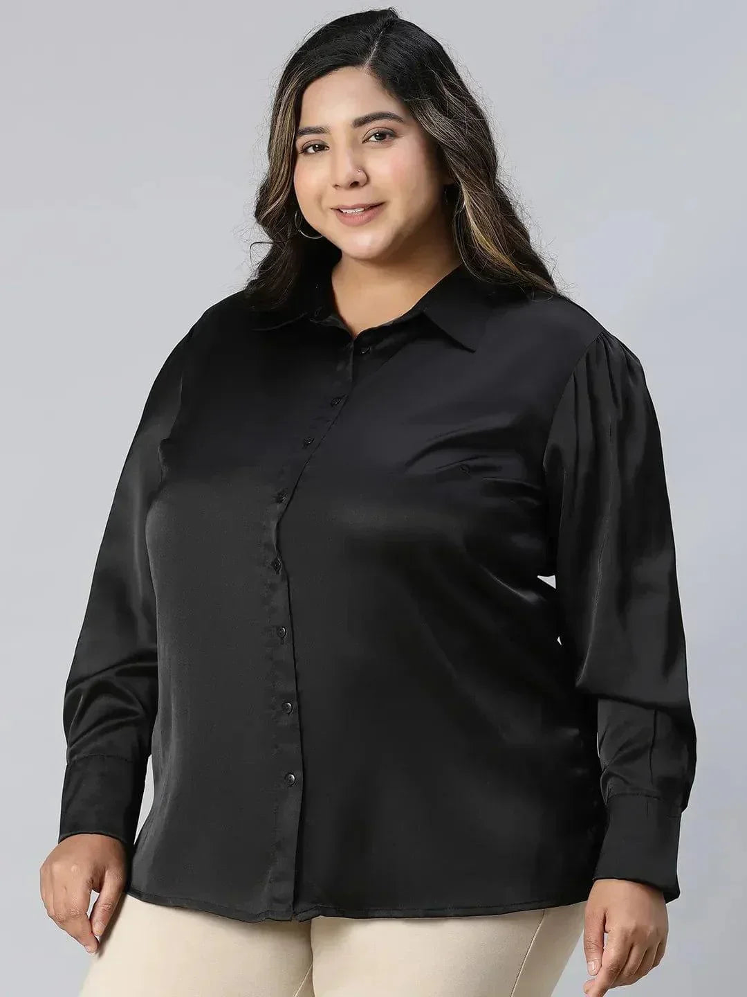 A woman with long, wavy brown hair wearing a black shirt and beige pants, smiling at the camera.