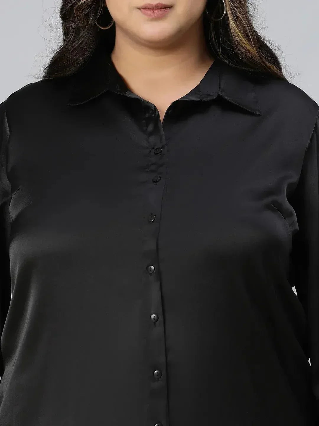 A woman with long, wavy brown hair wearing a black shirt and beige pants, smiling at the camera.
