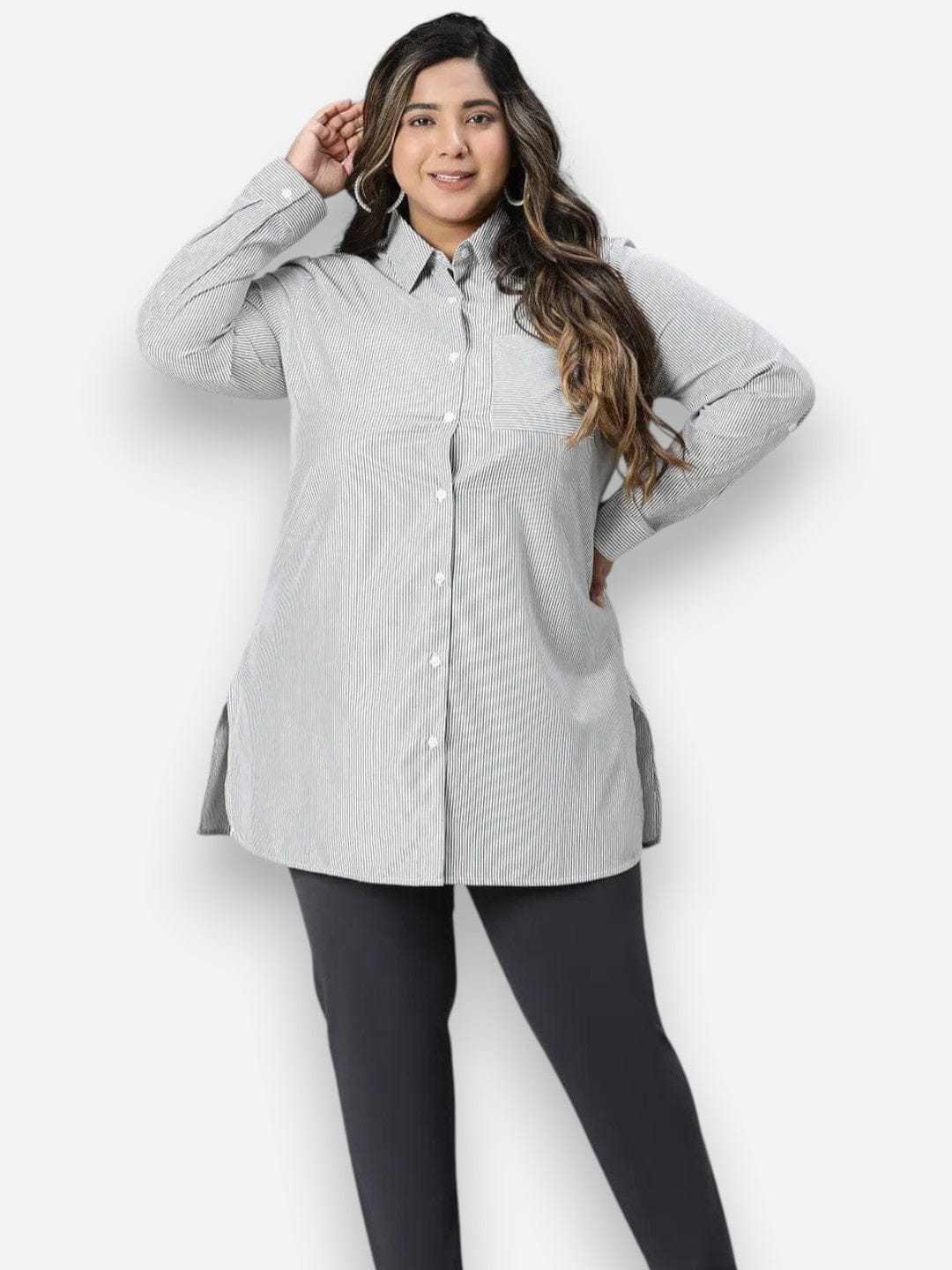 A woman with long brown hair wearing a gray striped shirt and dark pants is posing with her hand on her hip.
