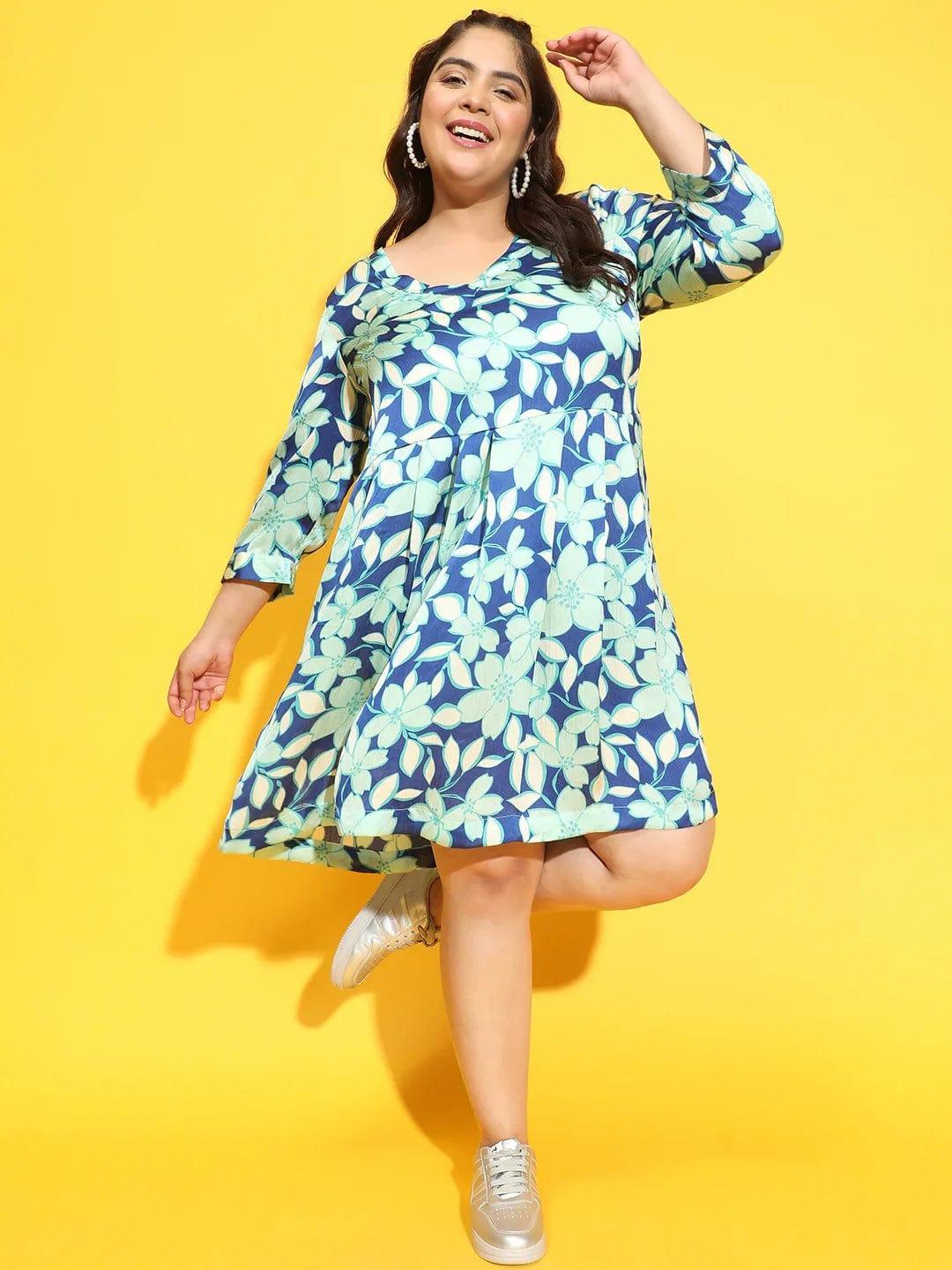 A woman wearing a blue and green floral print dress and silver sneakers is smiling at the camera.