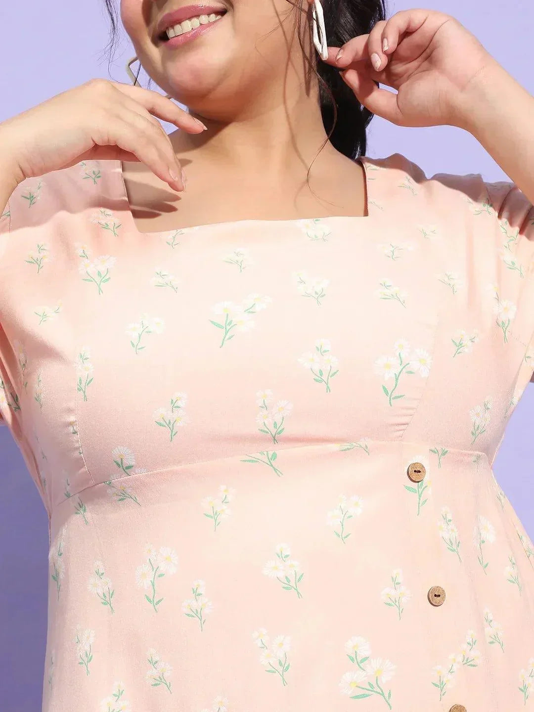 A woman wearing a pink dress with a floral pattern and white sneakers is smiling and posing for the camera.