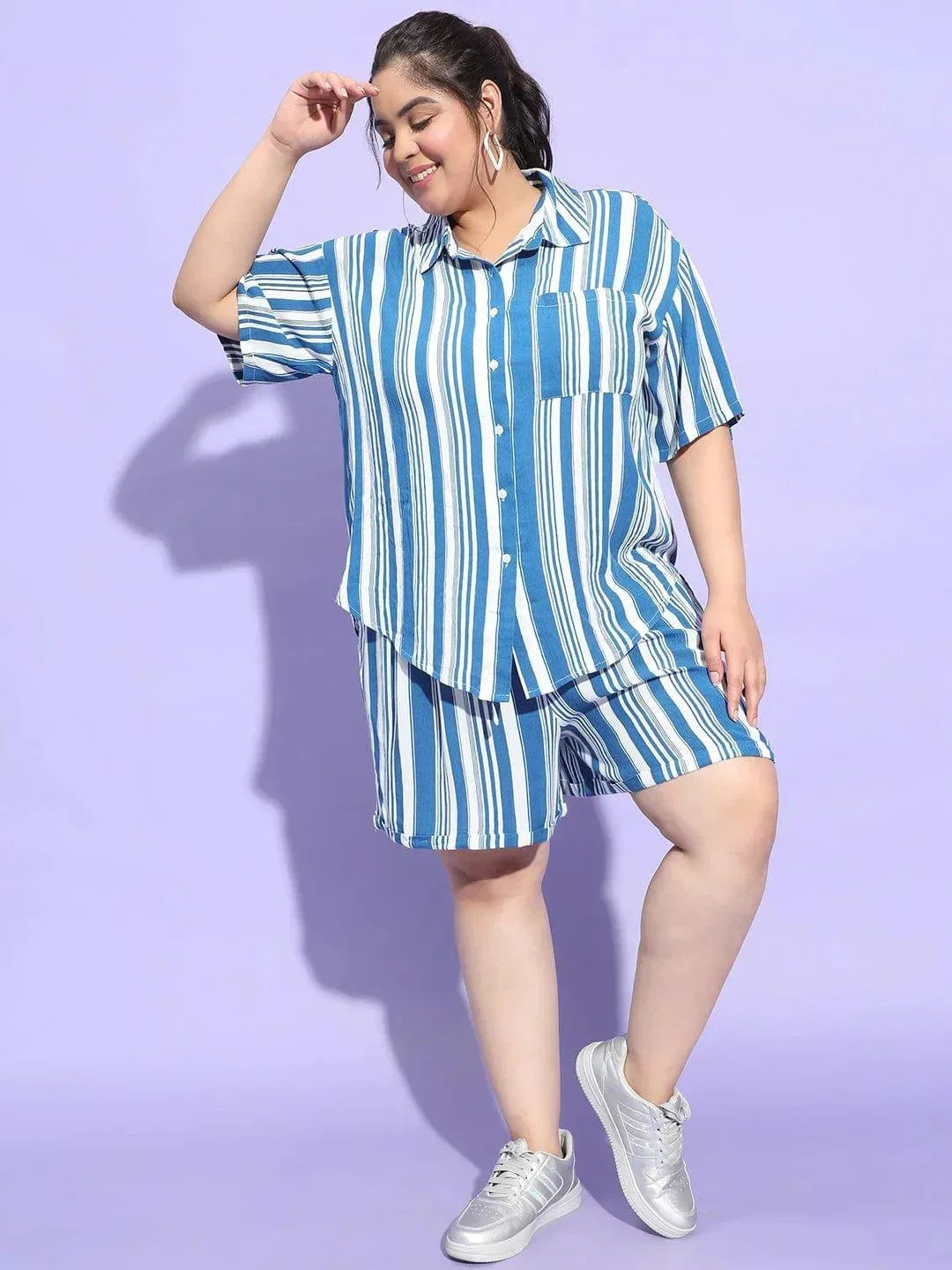 A woman wearing a blue and white striped shirt and shorts is smiling at the camera.