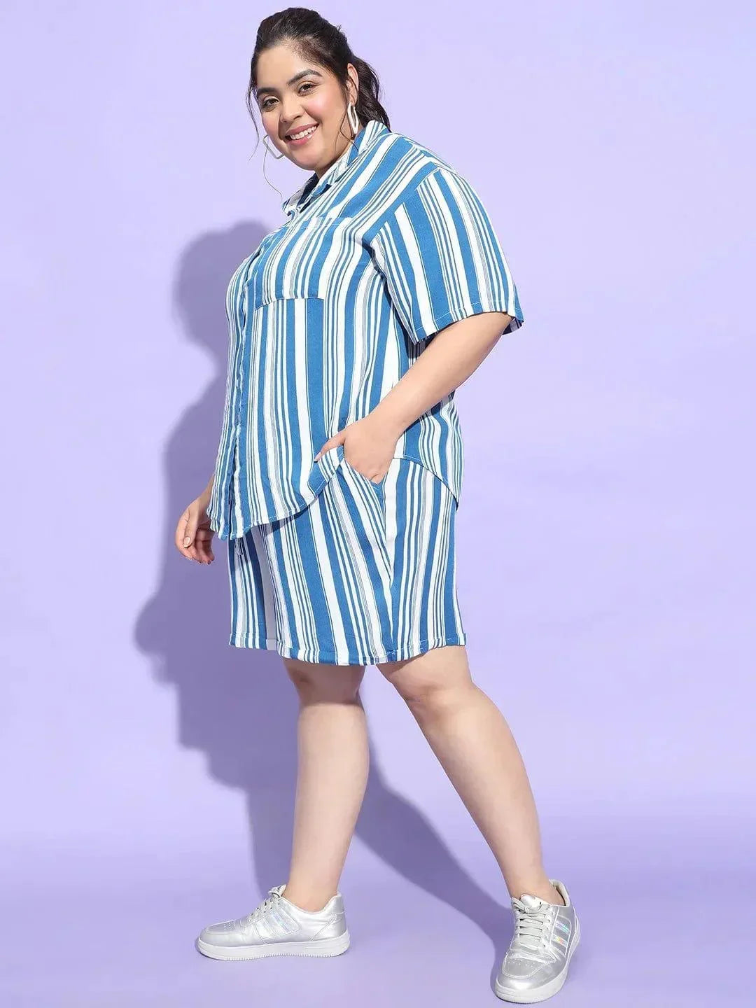 A woman wearing a blue and white striped shirt and shorts is smiling at the camera.