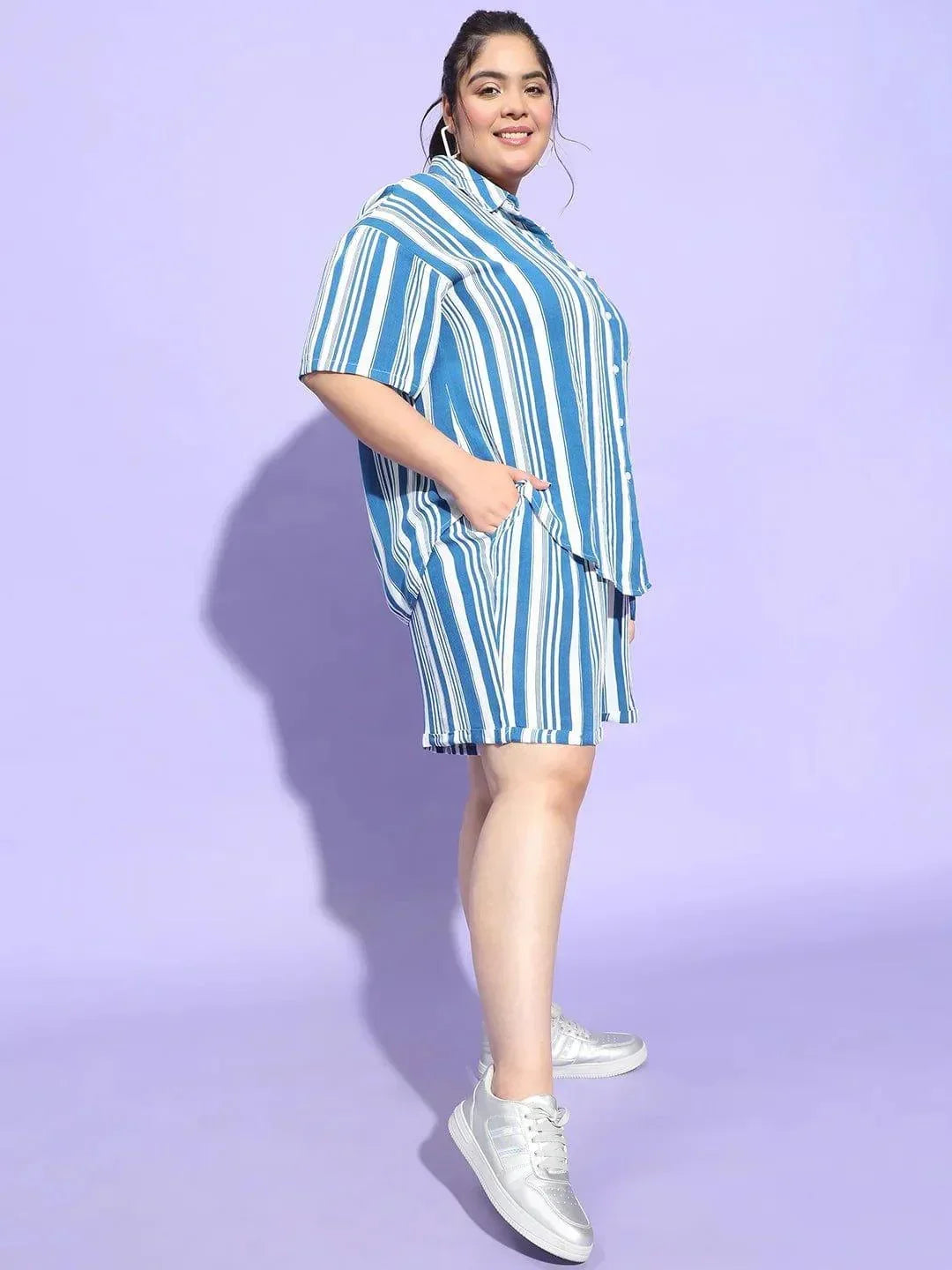 A woman wearing a blue and white striped shirt and shorts is smiling at the camera.
