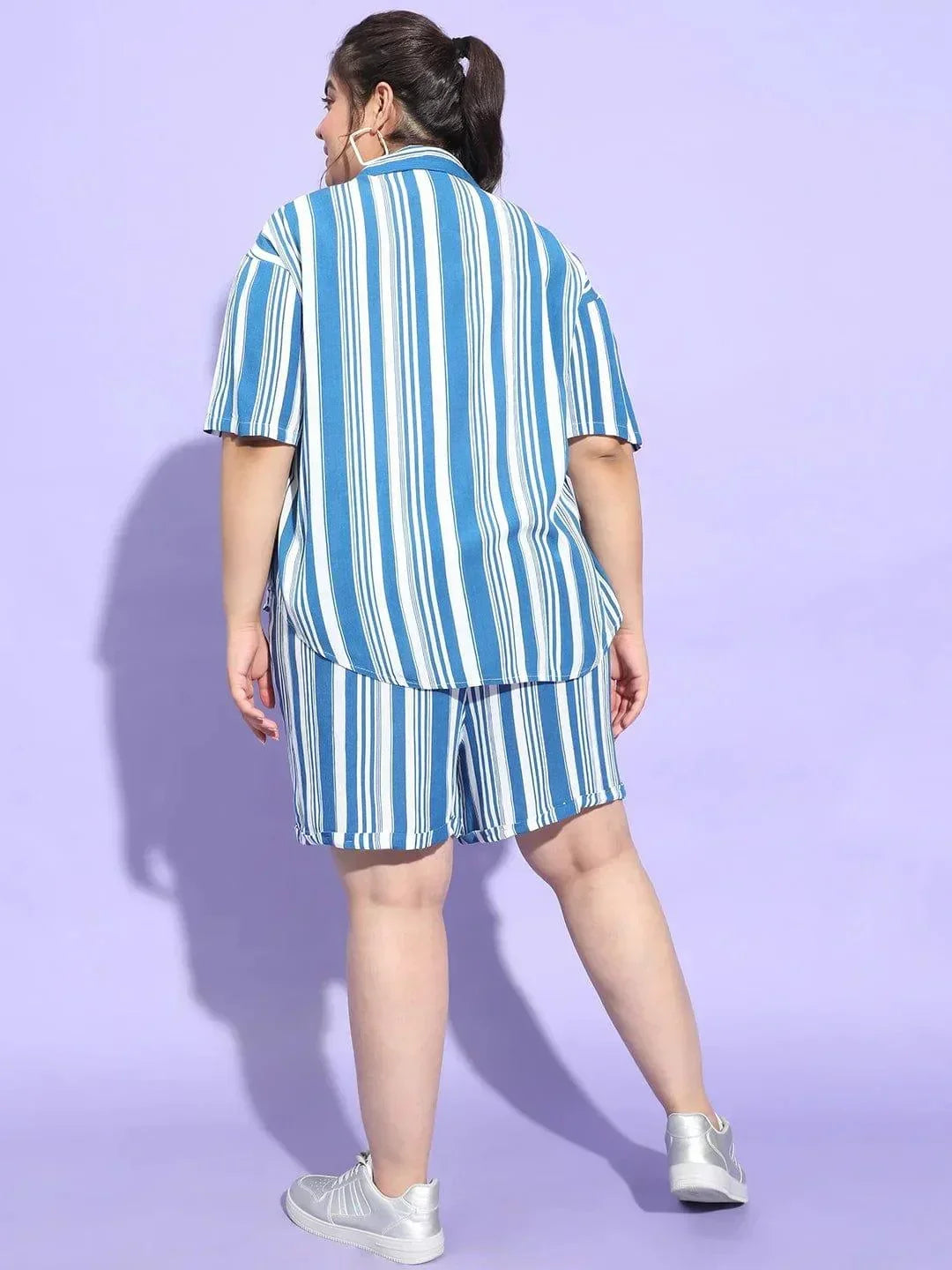 A woman wearing a blue and white striped shirt and shorts is smiling at the camera.