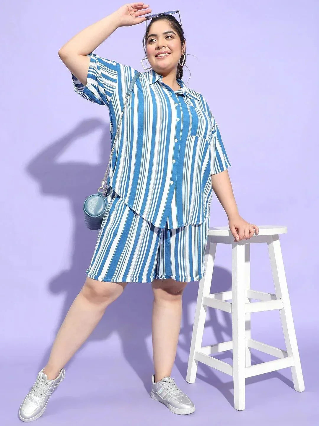 A woman wearing a blue and white striped shirt and shorts is smiling at the camera.