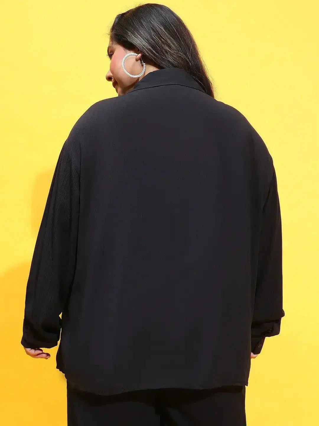 A woman wearing a black shirt and standing against a white background.