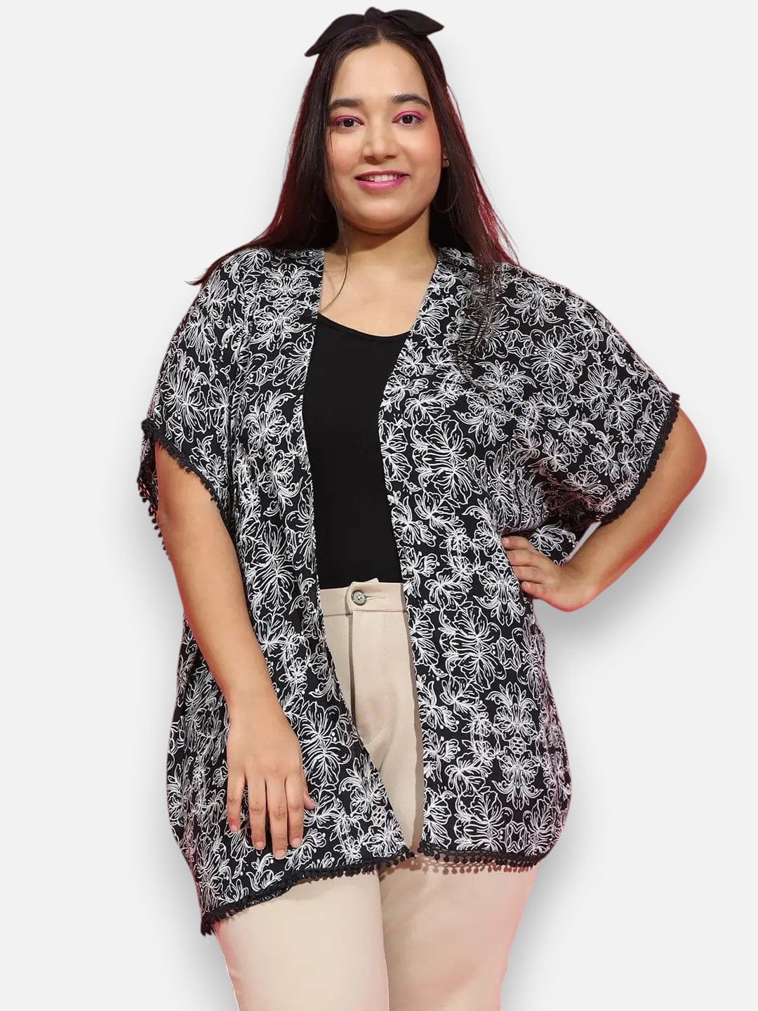 A woman with long dark hair wearing a black and white patterned cardigan and beige pants, smiling at the camera.