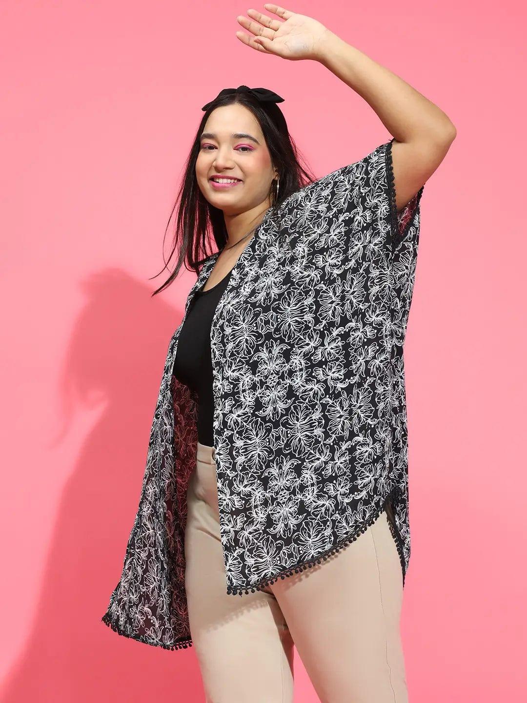 A woman with long dark hair wearing a black and white patterned cardigan and beige pants, smiling at the camera.