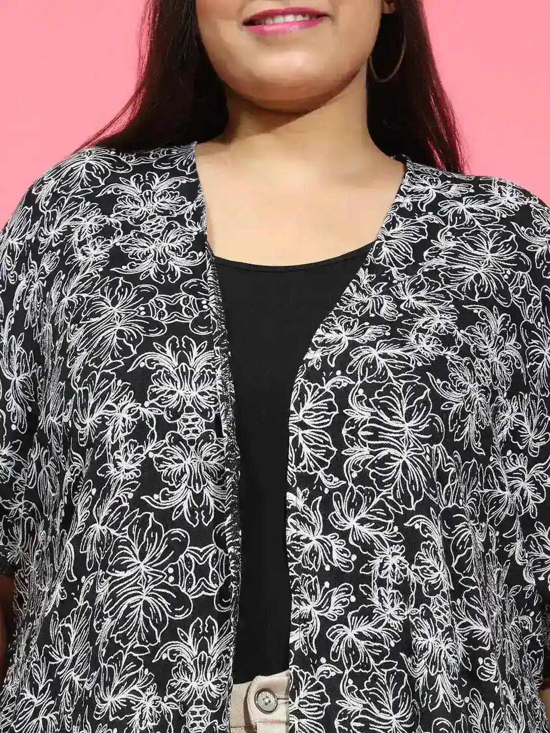 A woman with long dark hair wearing a black and white patterned cardigan and beige pants, smiling at the camera.