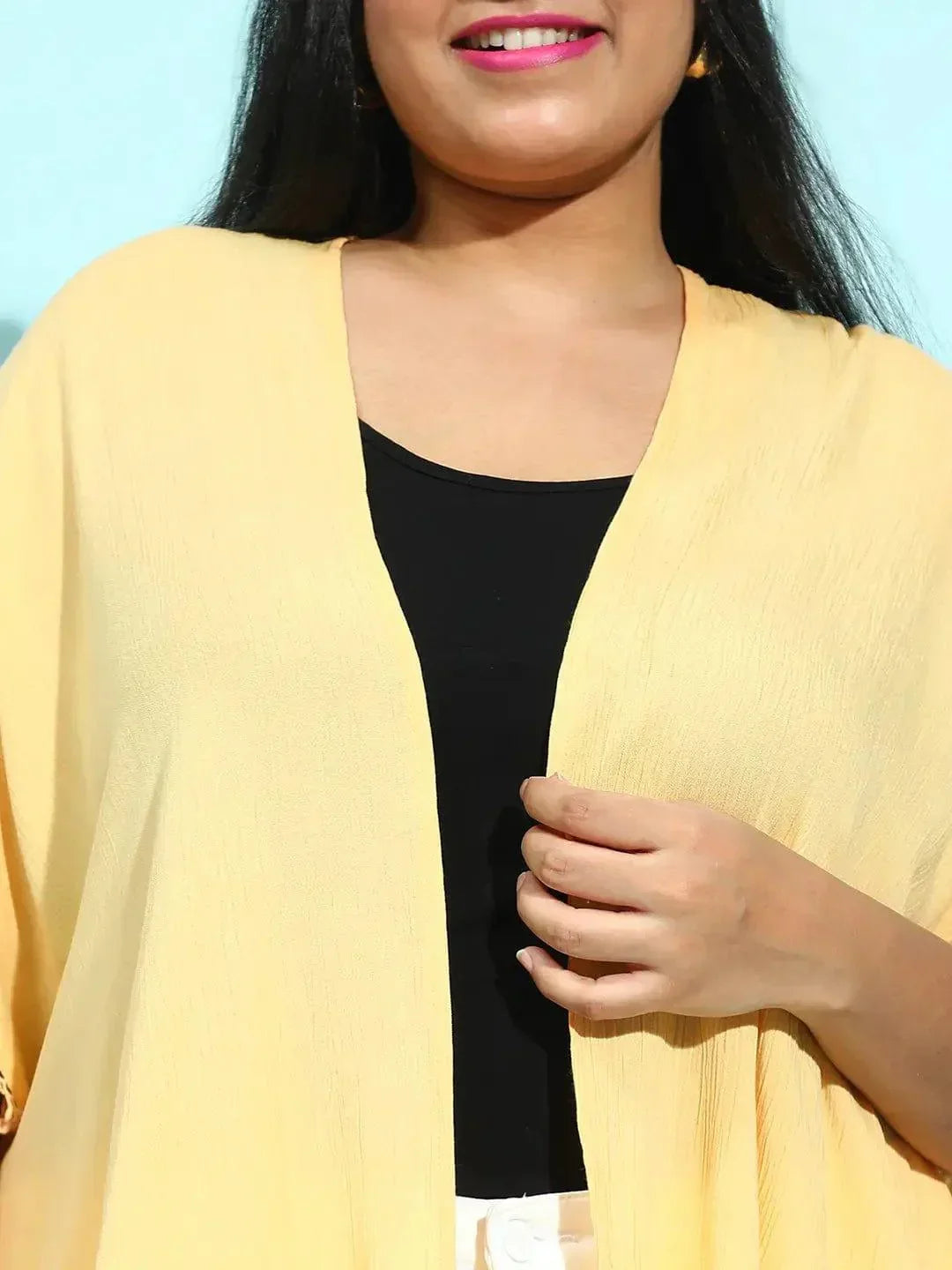 A woman with long dark hair wearing a yellow cardigan and a black top, smiling at the camera.