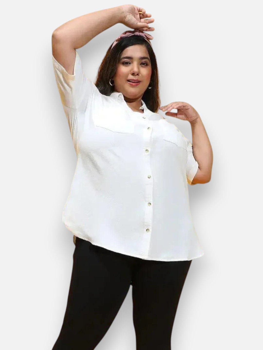 A woman wearing a white shirt and black pants is posing with her hands in her hair.