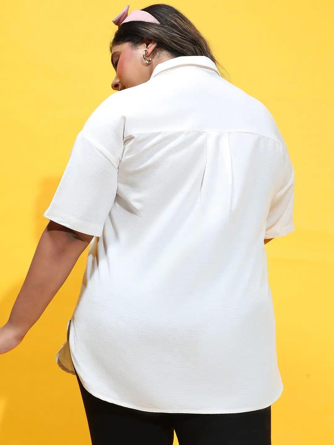 A woman wearing a white shirt and black pants is posing with her hands in her hair.