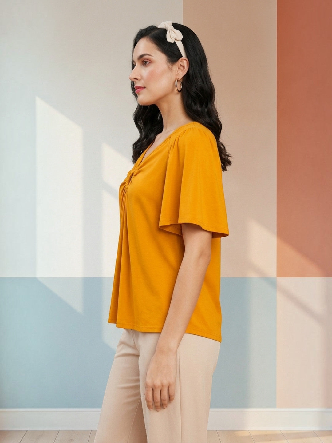 Mustard yellow women's top with ruched V-neck and short sleeves, paired with beige pants for casual fashion.