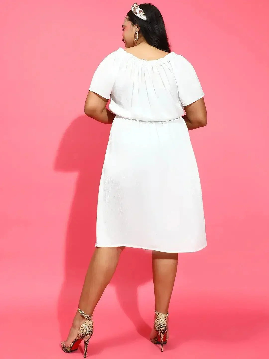 A woman wearing a white dress and high heels is smiling and posing for the camera.
