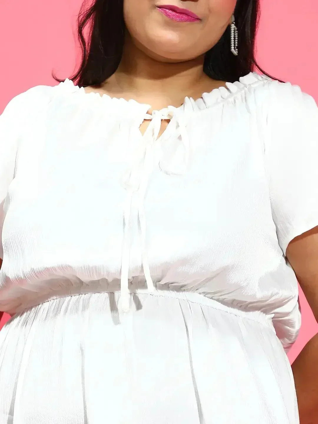 A woman wearing a white dress and high heels is smiling and posing for the camera.
