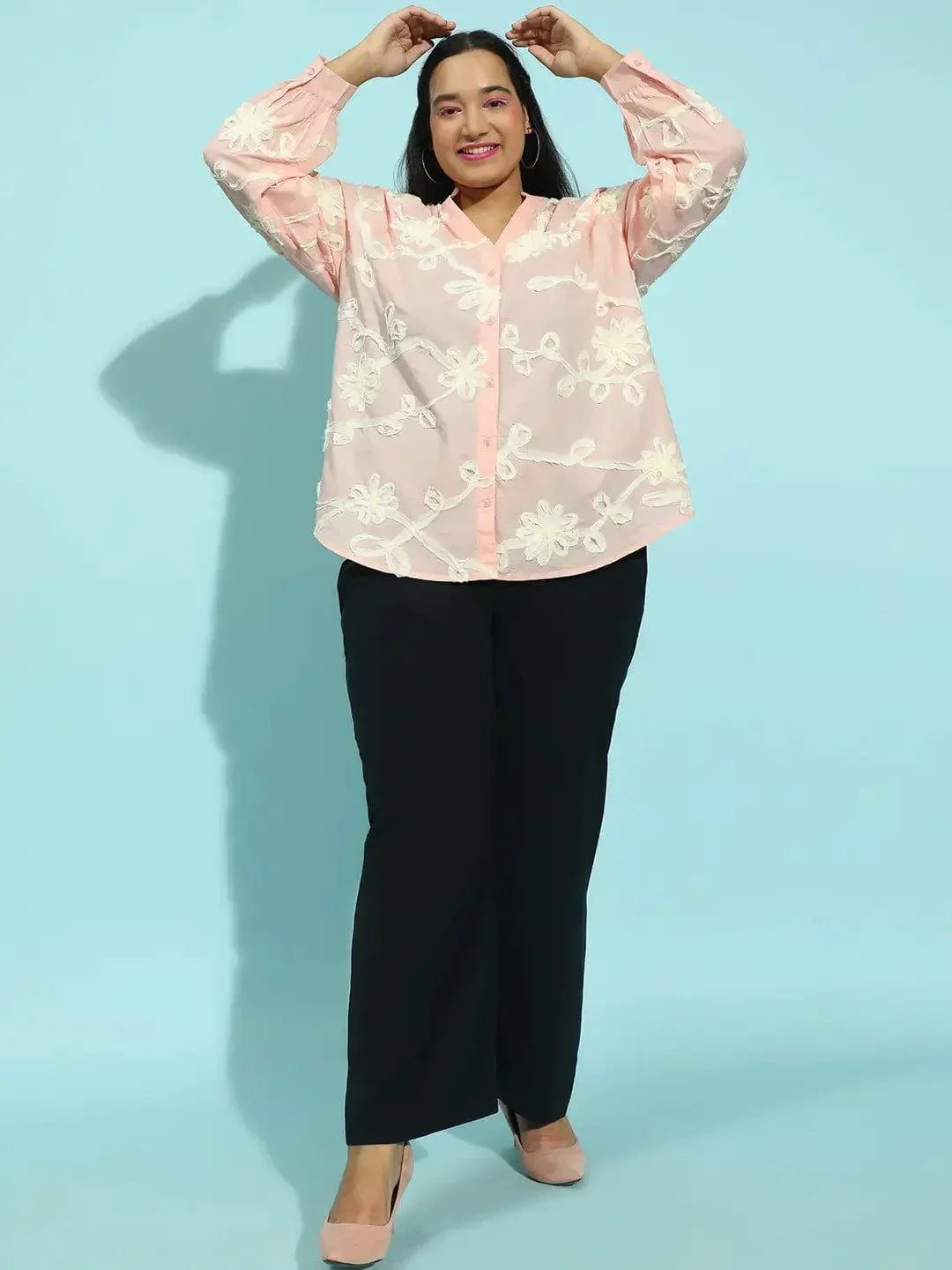 A woman with long dark hair wearing a pink blouse with white floral embroidery.