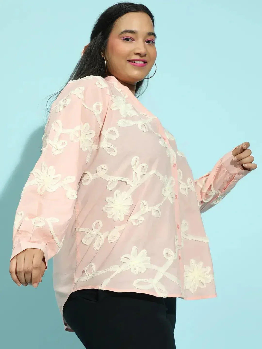 A woman with long dark hair wearing a pink blouse with white floral embroidery.