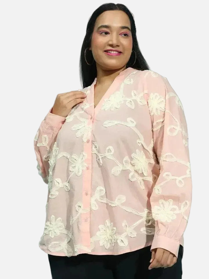 A woman with long dark hair wearing a pink blouse with white floral embroidery.