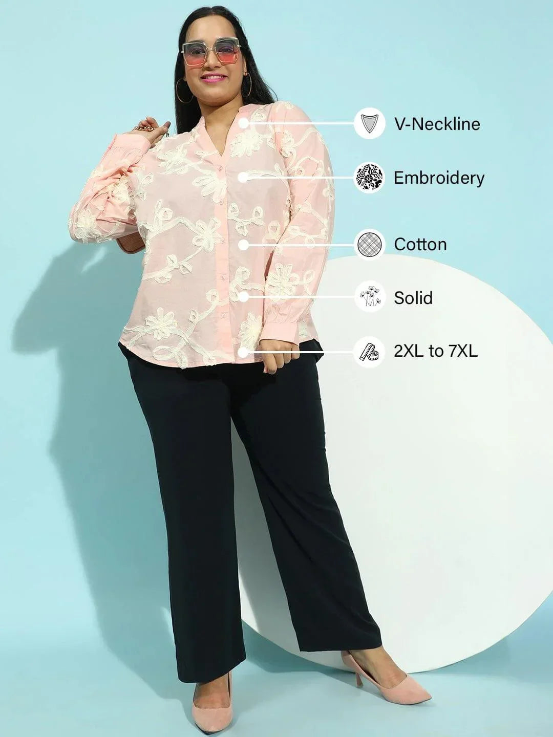 A woman with long dark hair wearing a pink blouse with white floral embroidery.