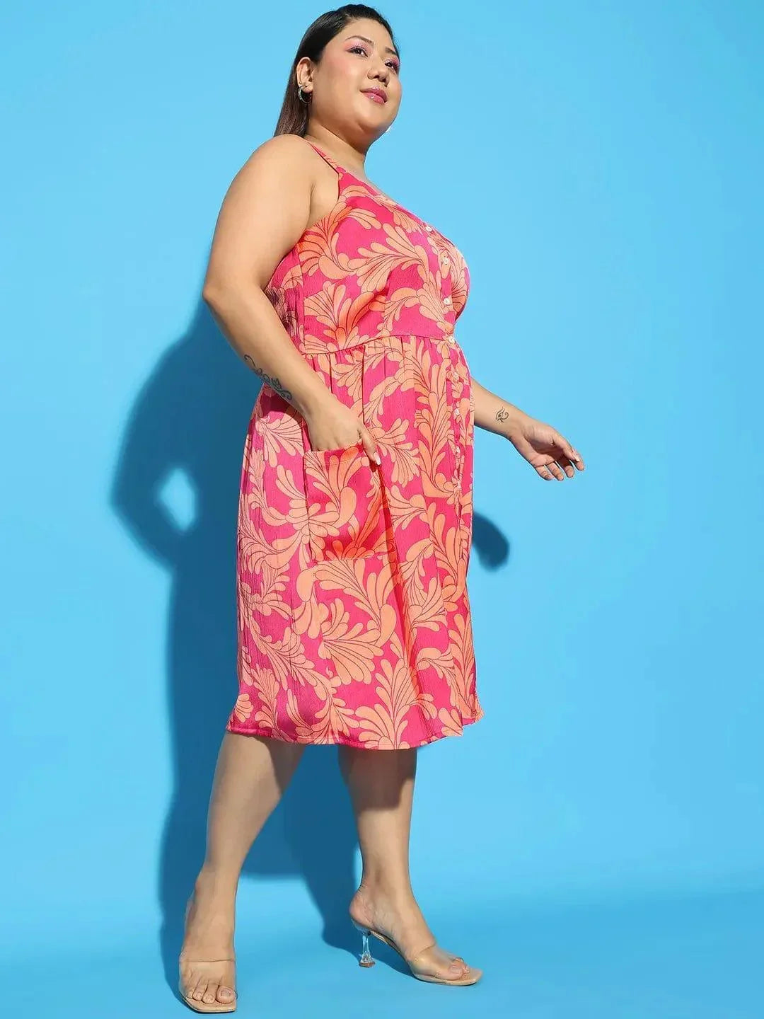 A woman wearing a pink floral print dress and holding a white purse stands against a white background.