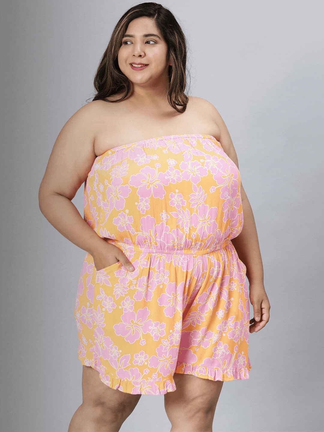 A smiling woman wearing a strapless, floral print dress stands against a white background.