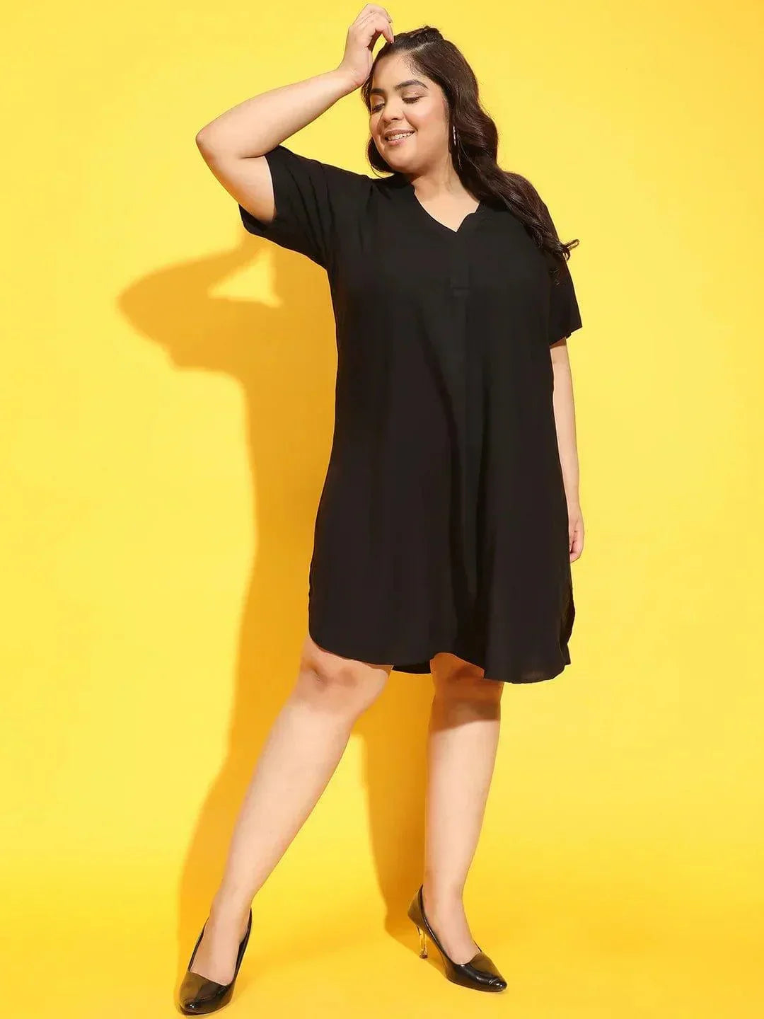 A woman wearing a black dress with a high neckline and short sleeves, smiling and posing for the camera.