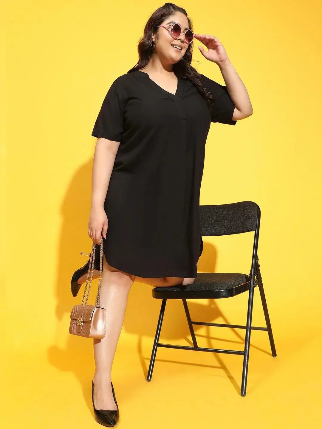 A woman wearing a black dress with a high neckline and short sleeves, smiling and posing for the camera.
