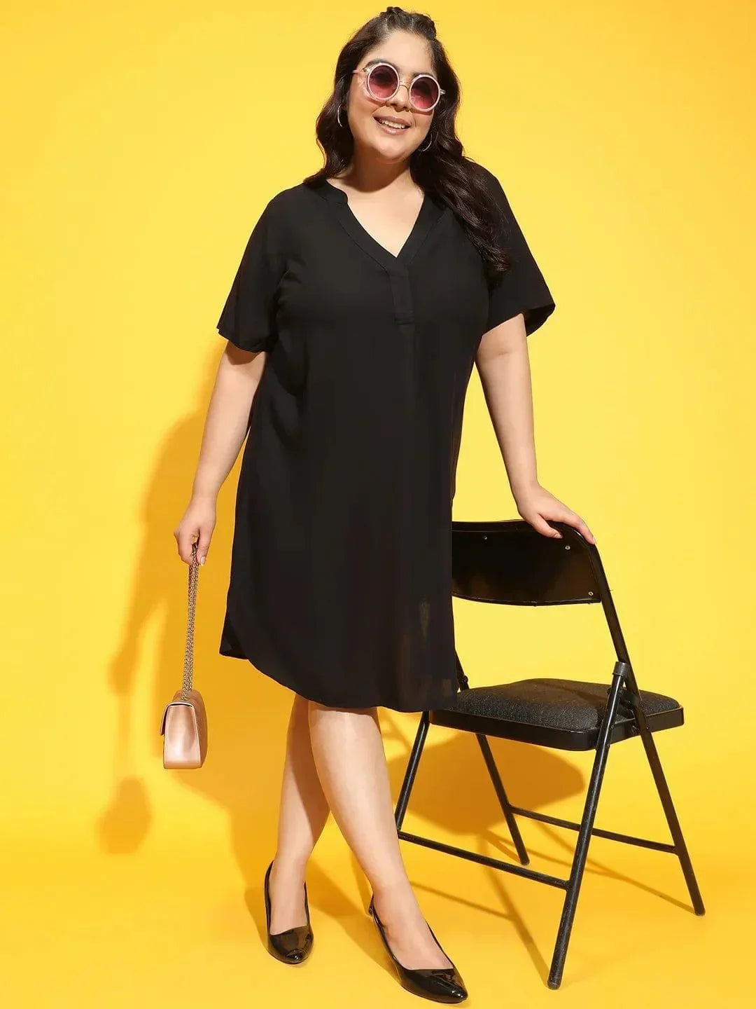 A woman wearing a black dress with a high neckline and short sleeves, smiling and posing for the camera.