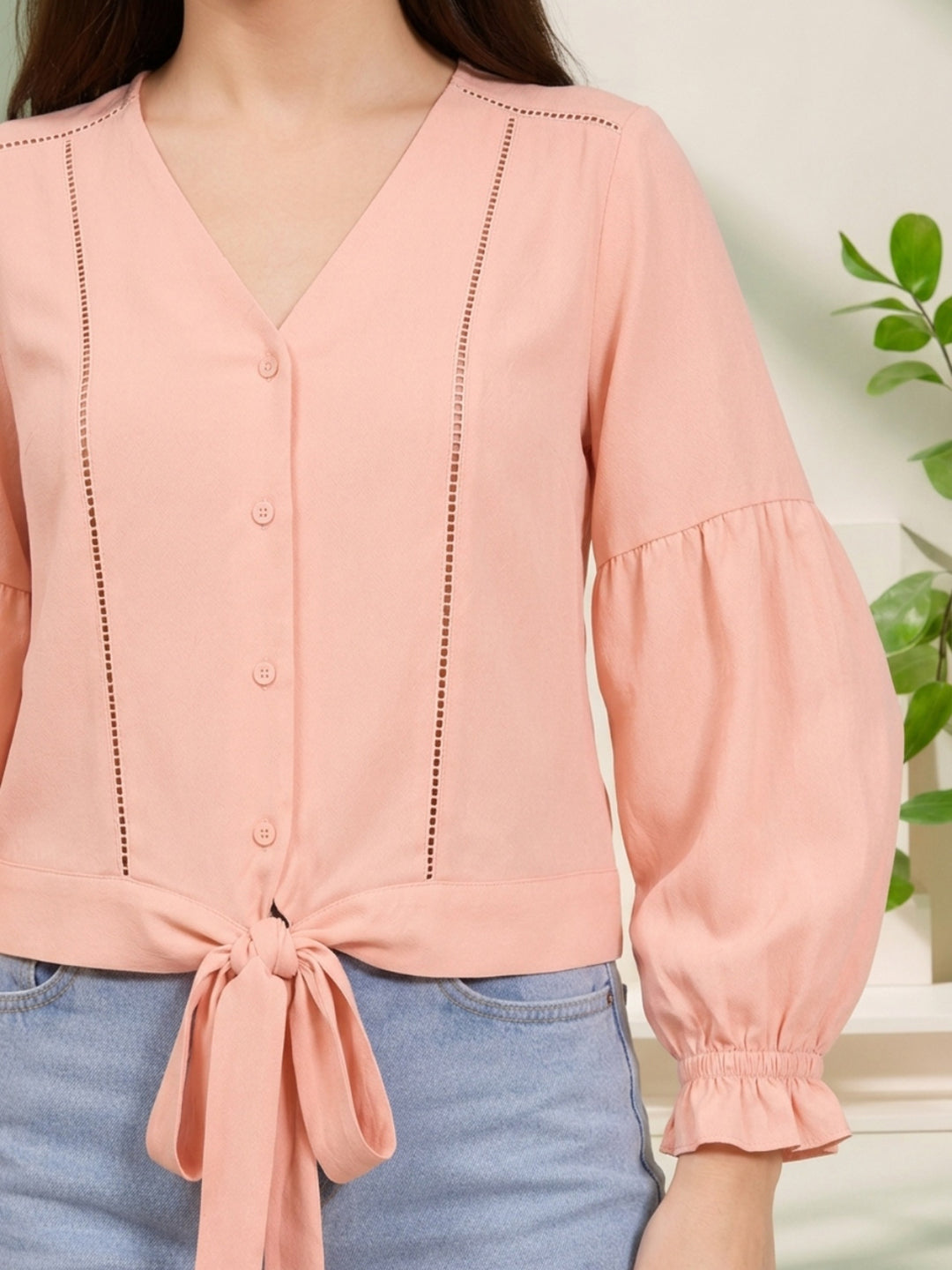 Pink tie-front blouse with puff sleeves and button details, paired with jeans