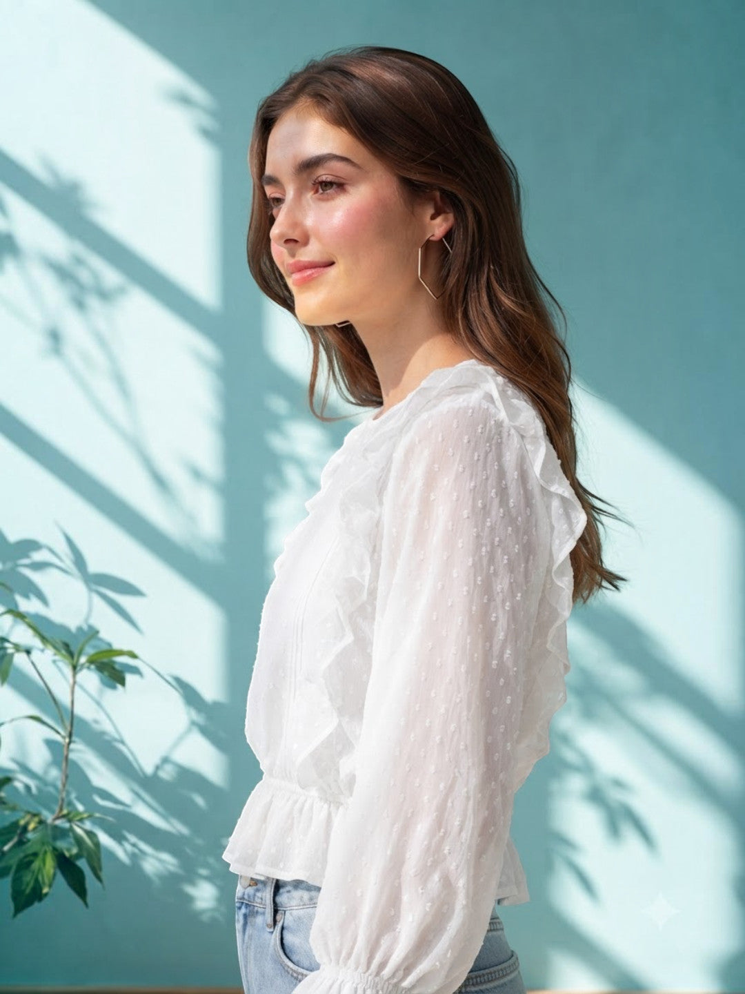 White ruffle blouse with sheer dot pattern, styled with jeans against teal wall with leaf shadows
