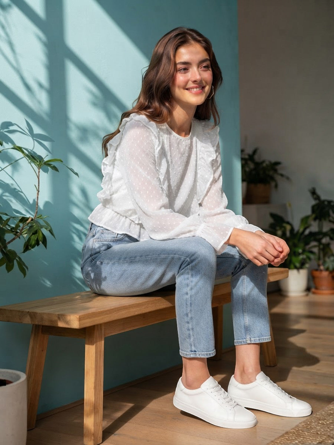 Woman in white ruffled blouse, light wash jeans, and white sneakers sitting on wooden bench