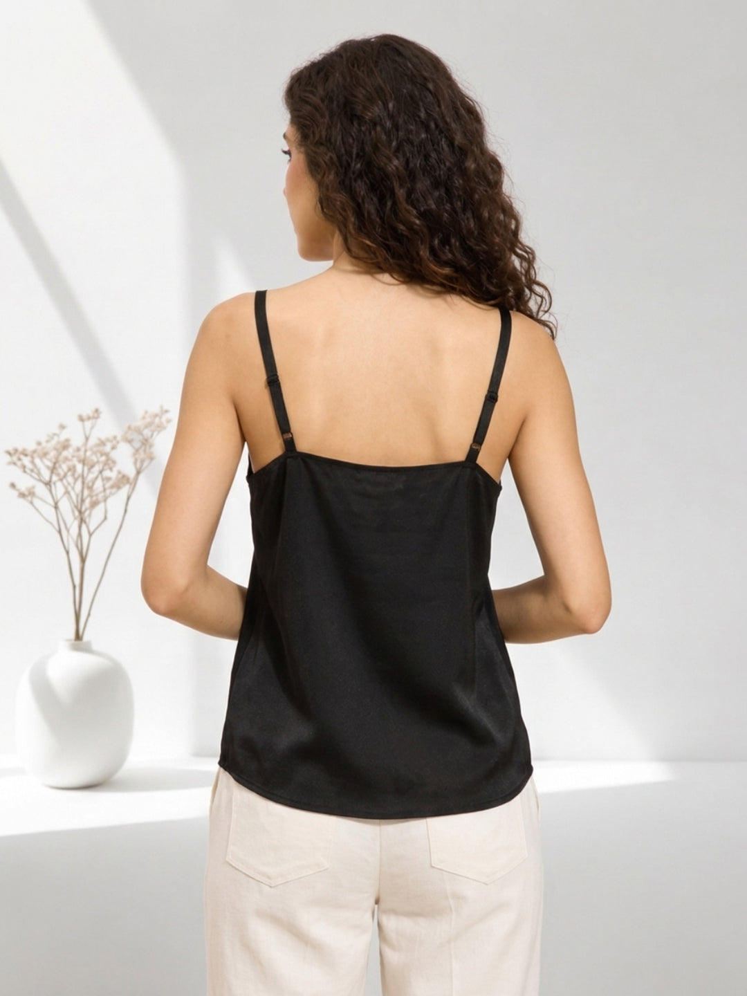 Black satin camisole top with adjustable straps, back view, paired with beige pants for women's fashion