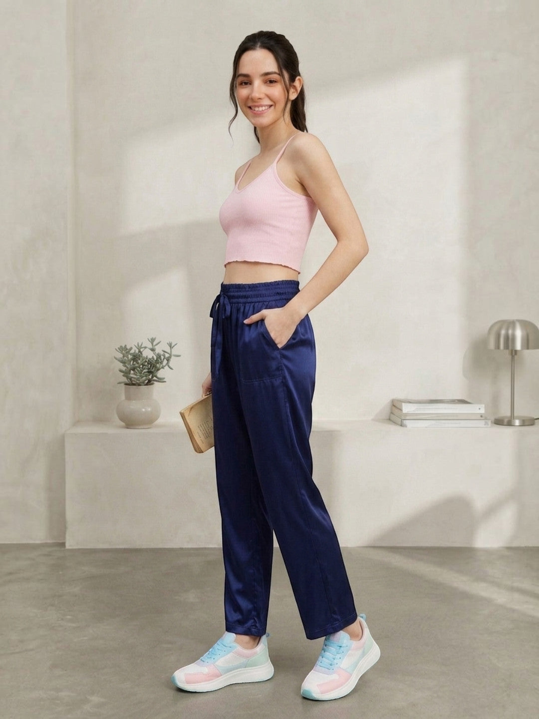 Woman in pink crop top and navy satin joggers, styled with pastel sneakers for casual comfort.