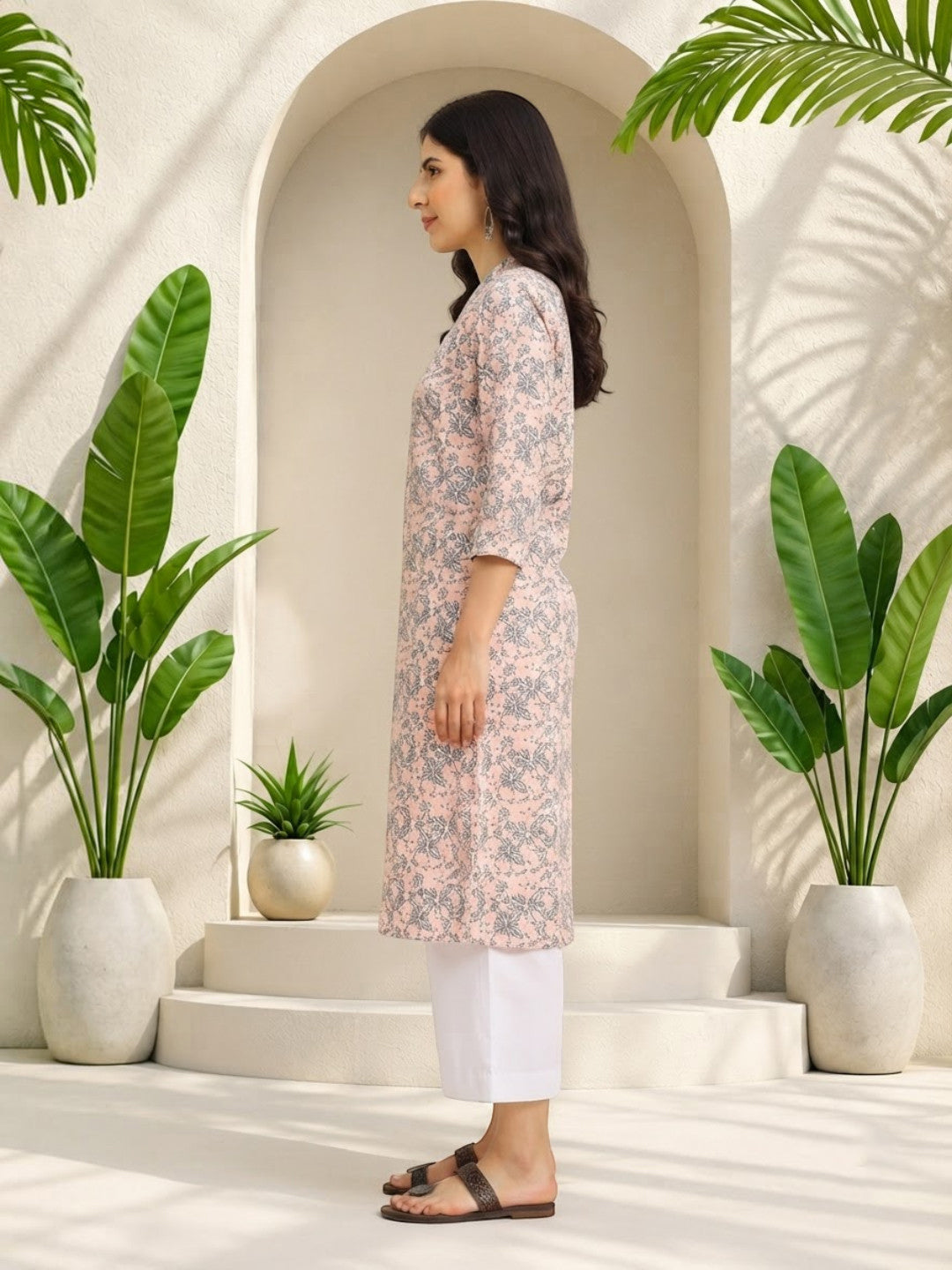Woman in pink floral kurta with white pants, styled for plus size & regular fashion, surrounded by green plants.