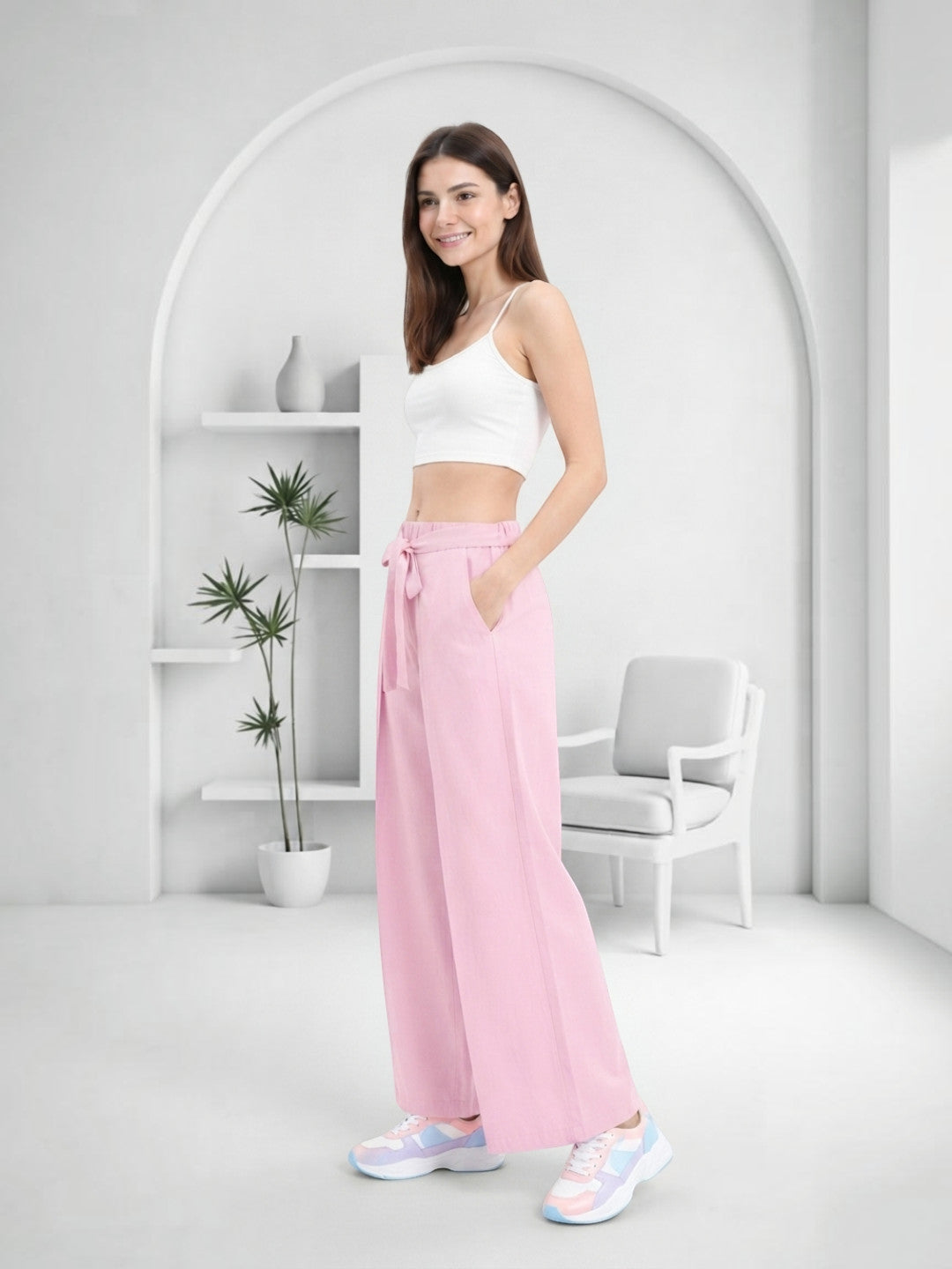 Woman in pink wide-leg pants with tie waist, white crop top, and pastel sneakers, styled for casual comfort.