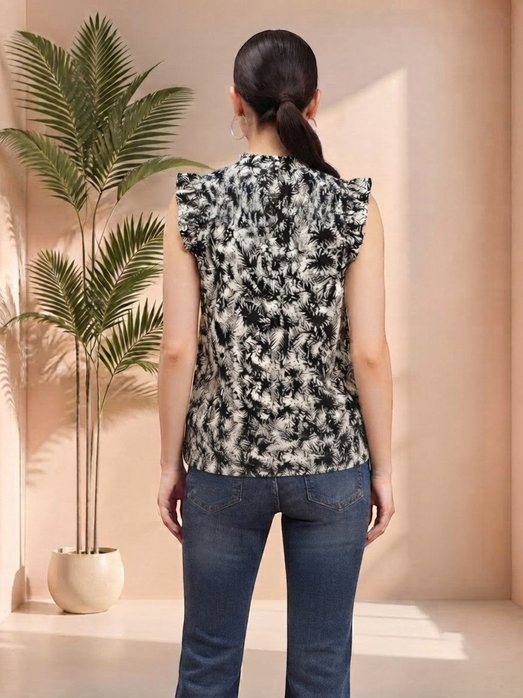 Woman wearing black and white floral print sleeveless top with ruffle shoulders, paired with blue jeans